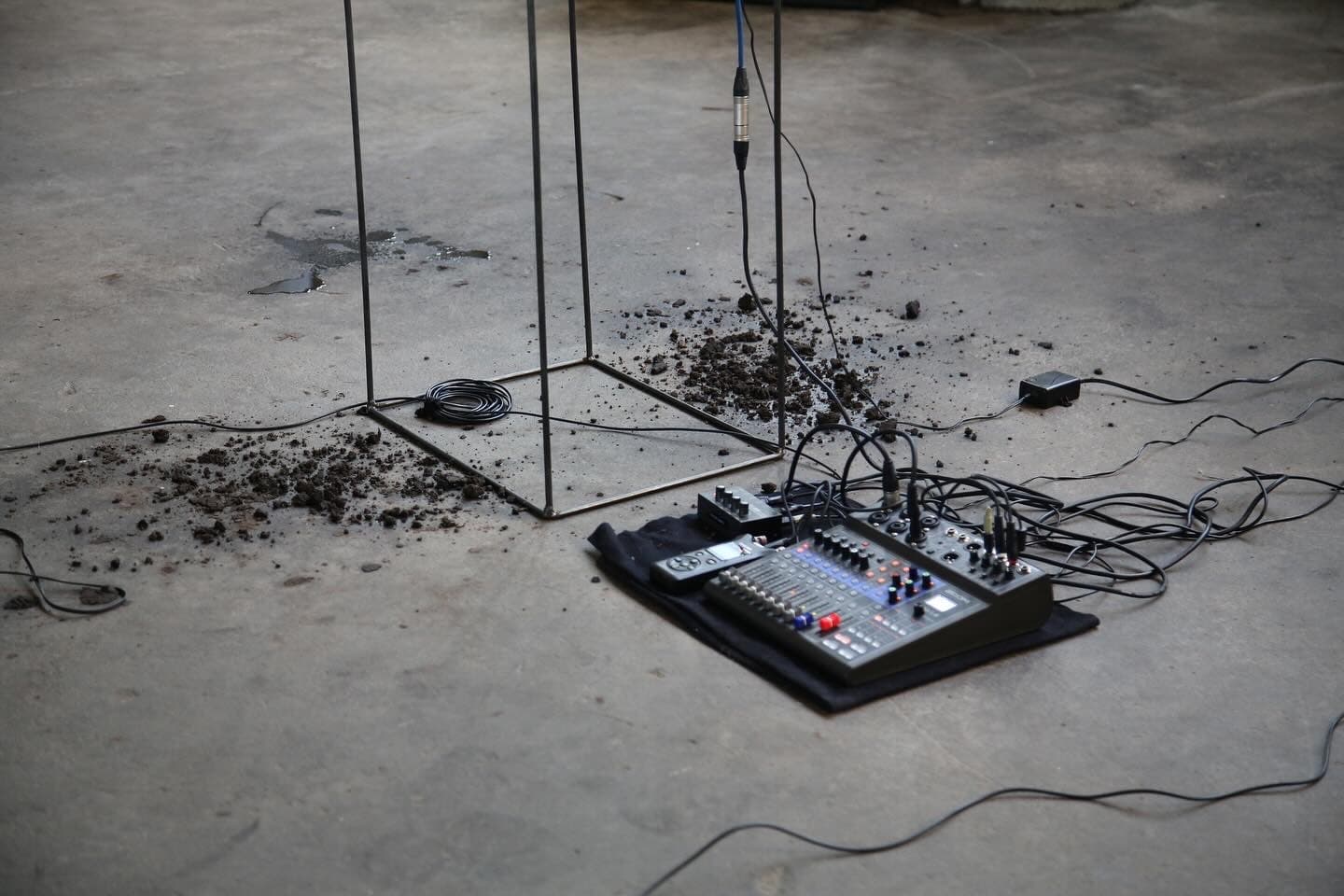 The image shows a synthesiser with many wires attached on the floor surrounded by soil.
