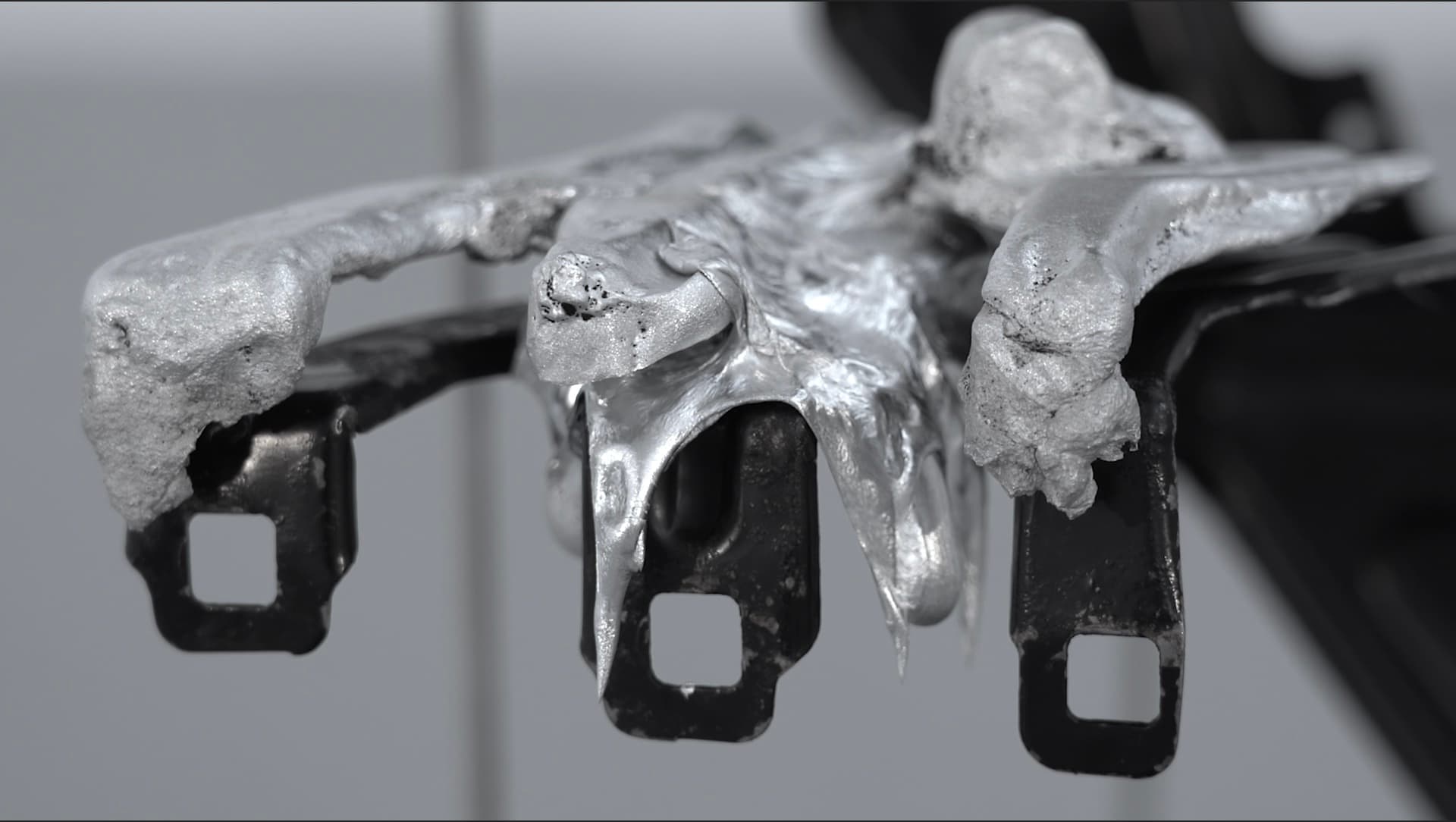 A close-up of a sculptural detail: solidified aluminium cast over black metal automotive components with square openings.