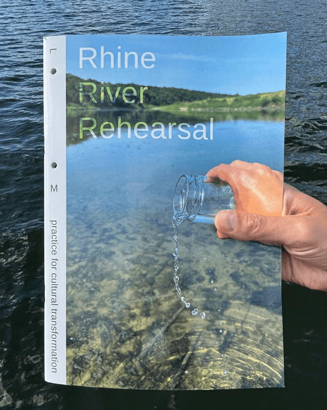 The image shows a publication with a river on the front of it, and a hand a pouring a glass of water into it.
