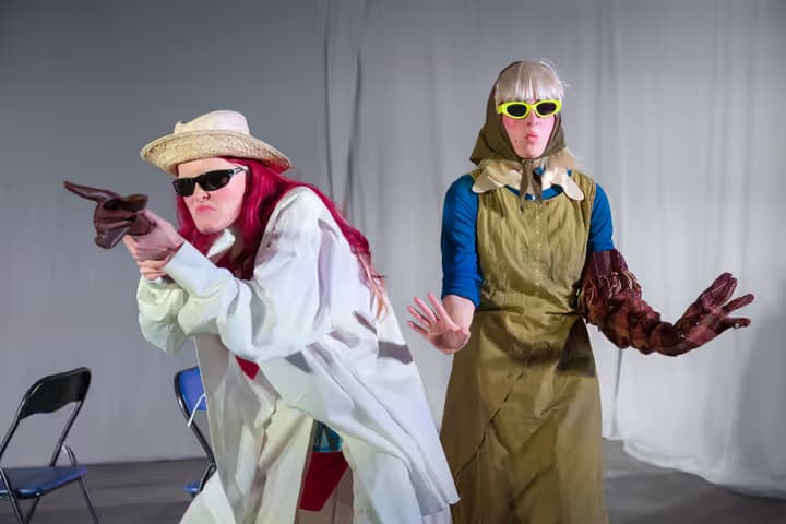 The image shows two people wearing hats, glasses, and coats performing.